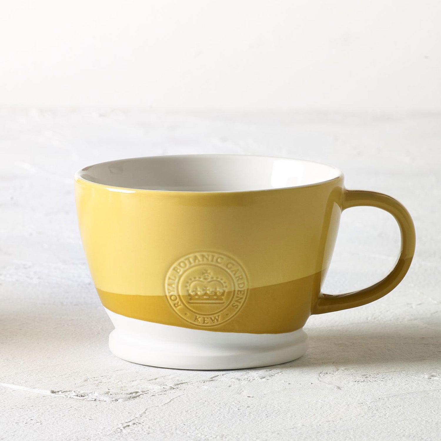 Mug with two sloping bands of yellow ocre, one large band of mid ocre and a smaller band below that of pale ocre on a white background, with white interior. From Kew Gardens available from Vinegar Hill.
