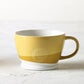 Mug with two sloping bands of yellow ocre, one large band of mid ocre and a smaller band below that of pale ocre on a white background, with white interior. From Kew Gardens available from Vinegar Hill.