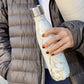 By Swell, this bottle features the beautiful patterns of Calacutta Gold Quartz with a high-gloss finish that mimics the lustre and sheen of the real stone.  Held by a model in puffa jacket.