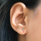 A gold plated multi coloured crystal bar ear stud by Lisa Angel from Vinegar Hill. Shown being worn vertically in a model’s ear lobe. From top to bottom they are - amethyst purple, sapphire blue, aqua marine blue, emerald green, diamante, citrine orange and ruby red. 